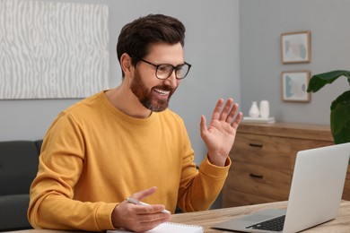 Photo of Man greeting someone during video chat via laptop at home