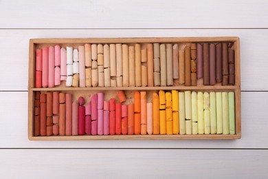 Photo of Set of soft pastels in box on white wooden table, top view. Drawing material