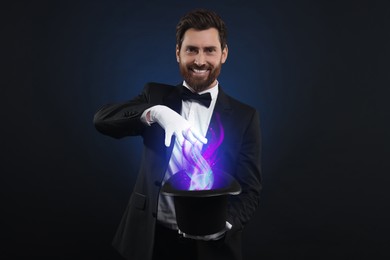 Magician showing trick with fantastic light coming out of top hat on dark background