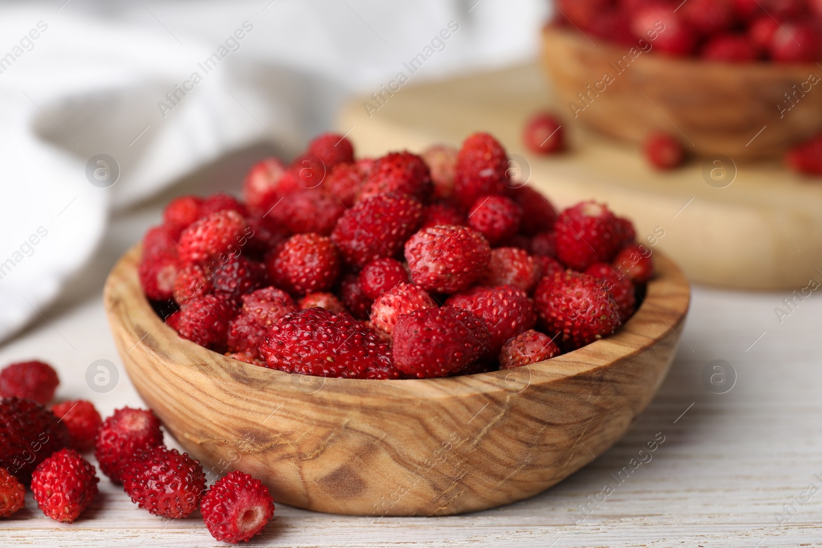 Photo of Fresh wild strawberries in bowl on white wooden table, closeup