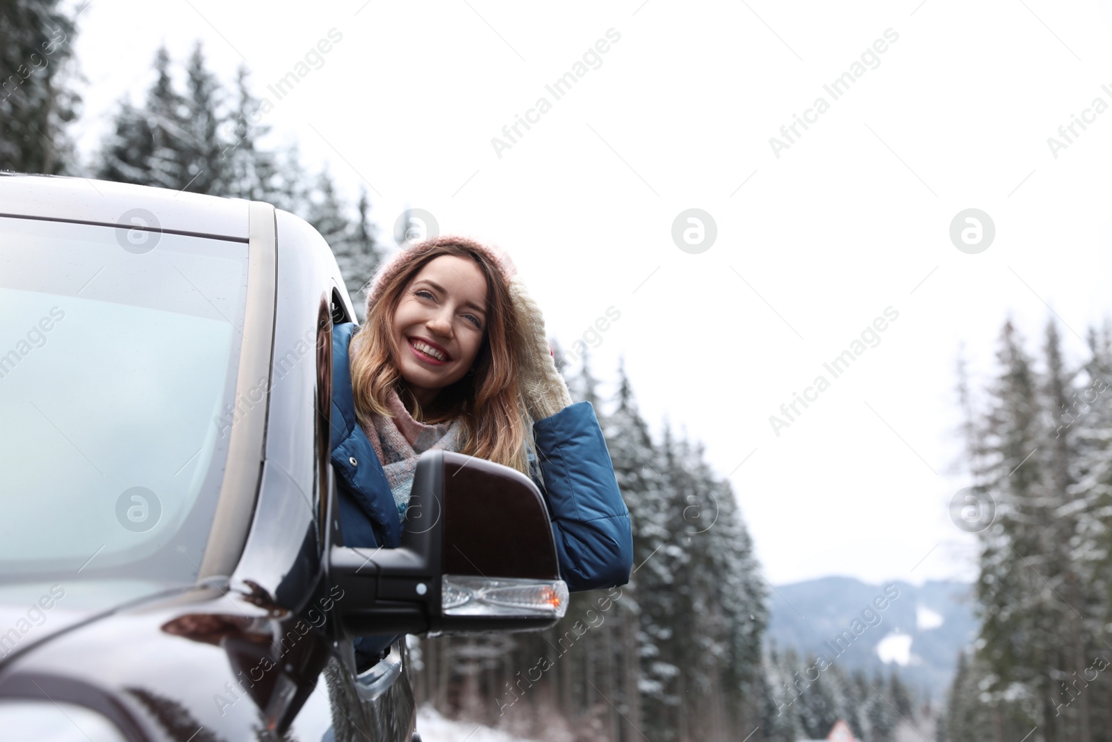 Photo of Young woman driving car and looking out of window on road. Winter vacation