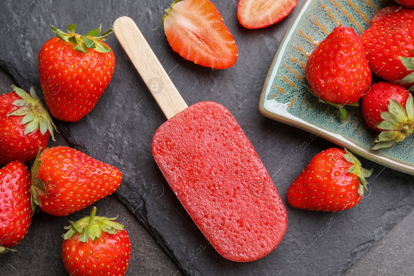 Photo of Tasty strawberry ice pop on dark table, flat lay. Fruit popsicle