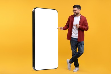 Image of Man pointing at huge mobile phone with empty screen on orange background. Mockup for design