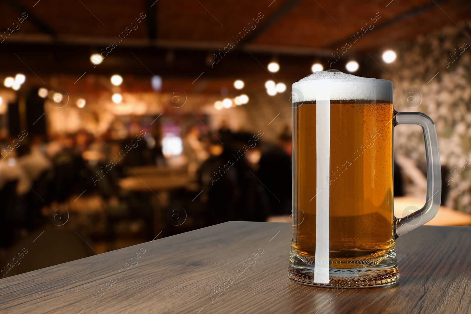 Image of Mug with fresh beer on wooden table in pub, space for text