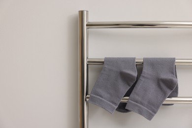 Heated towel rail with socks on white wall, closeup. Space for text