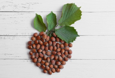 Photo of Hazelnuts and branch with leaves in shape of nut on white wooden table, flat lay