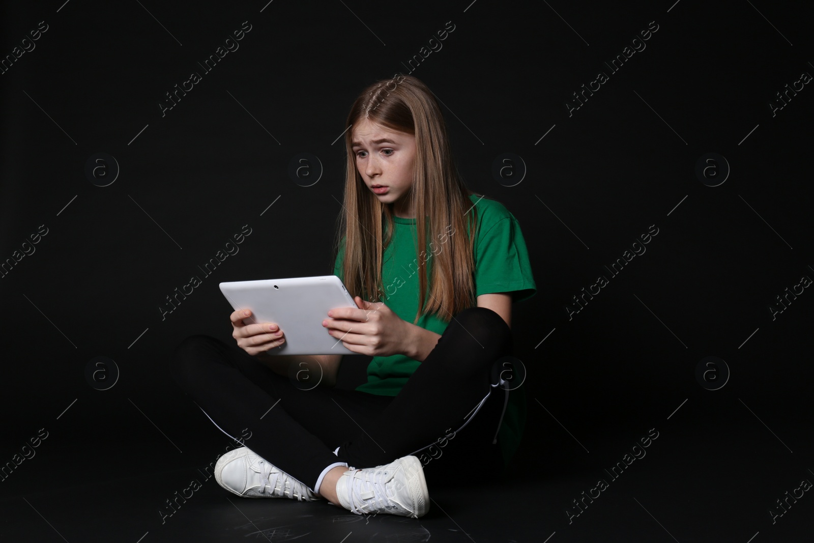 Photo of Shocked teenage girl with tablet on black background. Danger of internet