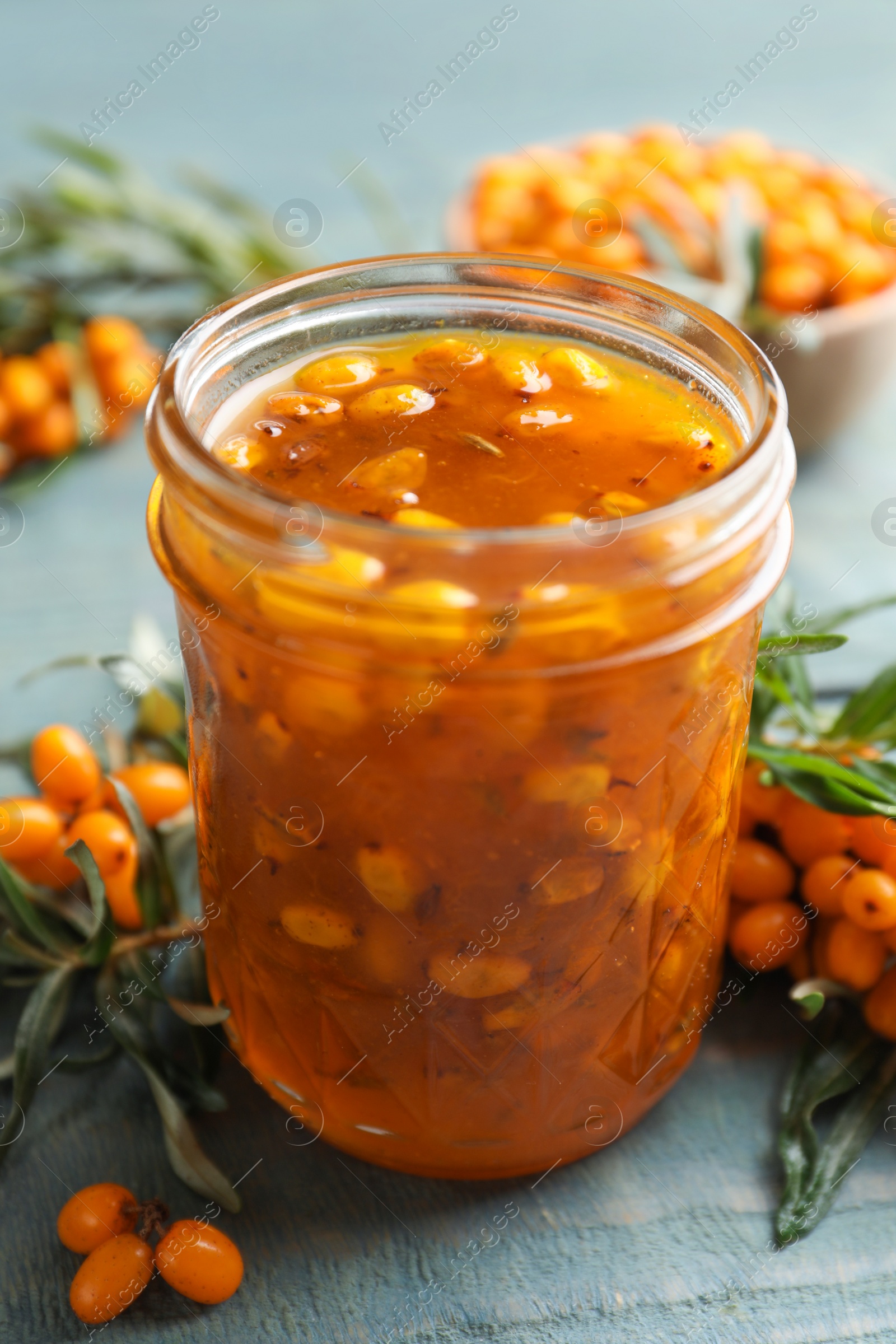 Photo of Delicious sea buckthorn jam and fresh berries on blue wooden table