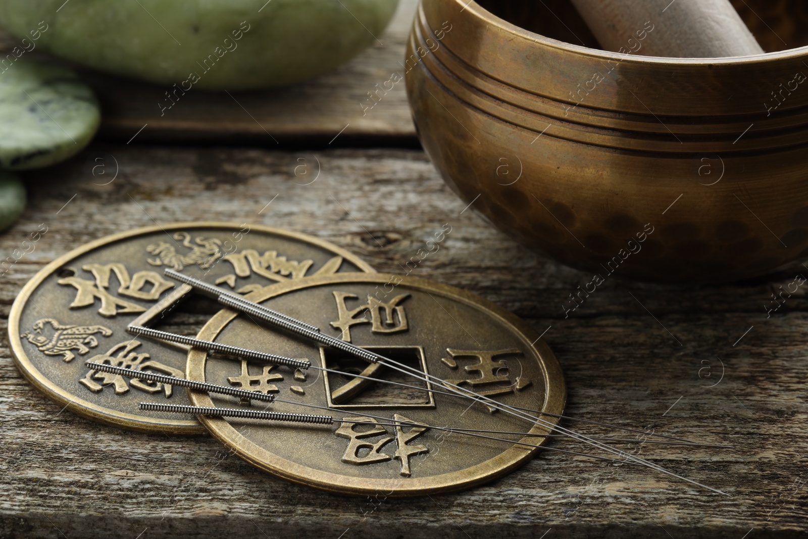 Photo of Acupuncture needles, Chinese coins and singing bowl on wooden table, closeup