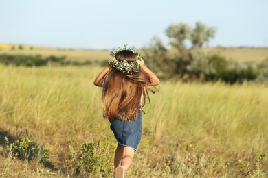 Photo of Cute little girl wearing flower wreath outdoors, back view. Child spending time in nature