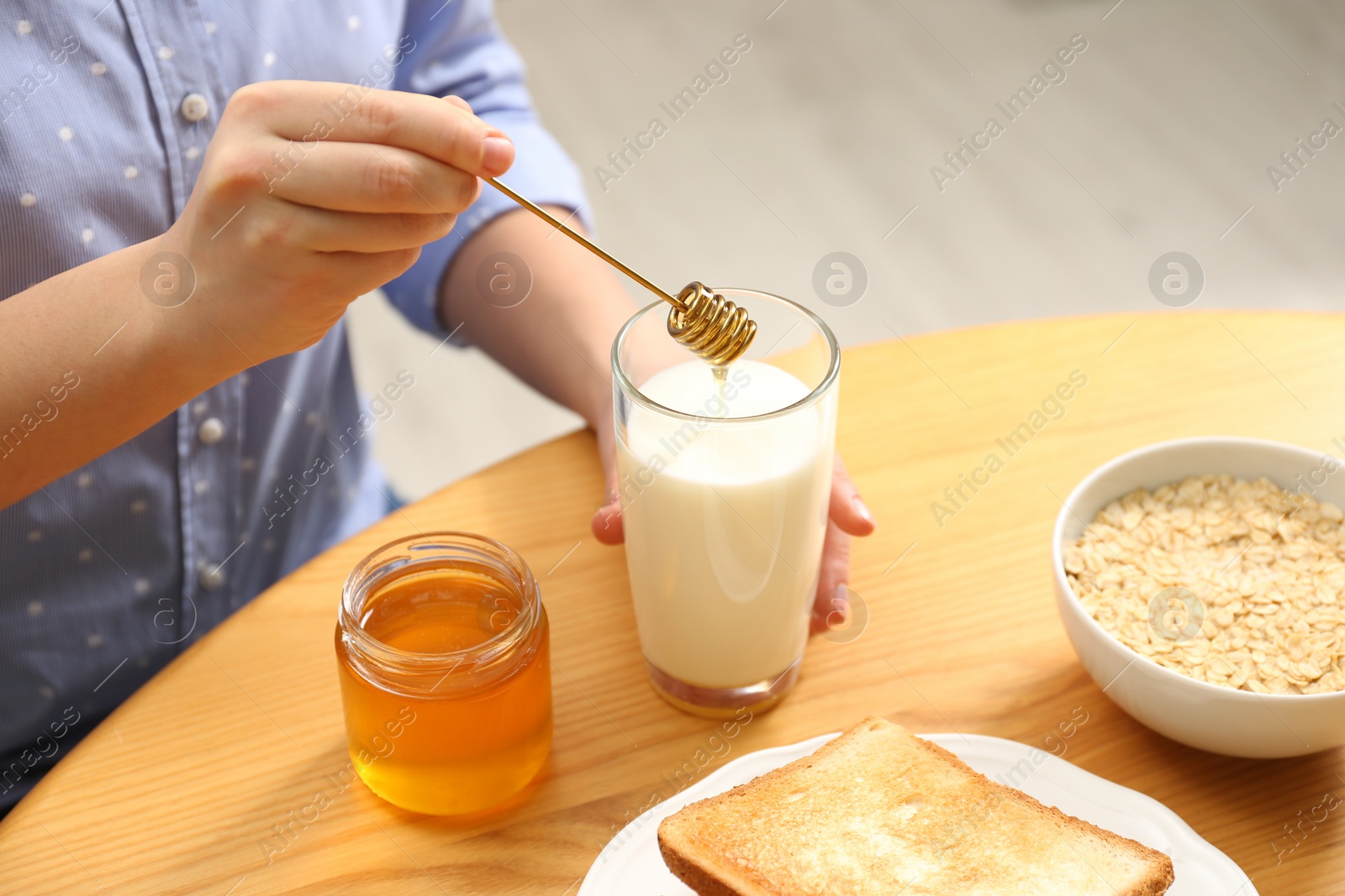 Photo of Woman adding honey to milk at table, closeup