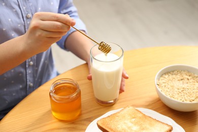 Photo of Woman adding honey to milk at table, closeup