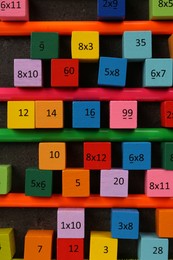 Many colorful cubes with numbers, multiplications and pencils on dark grey table, flat lay
