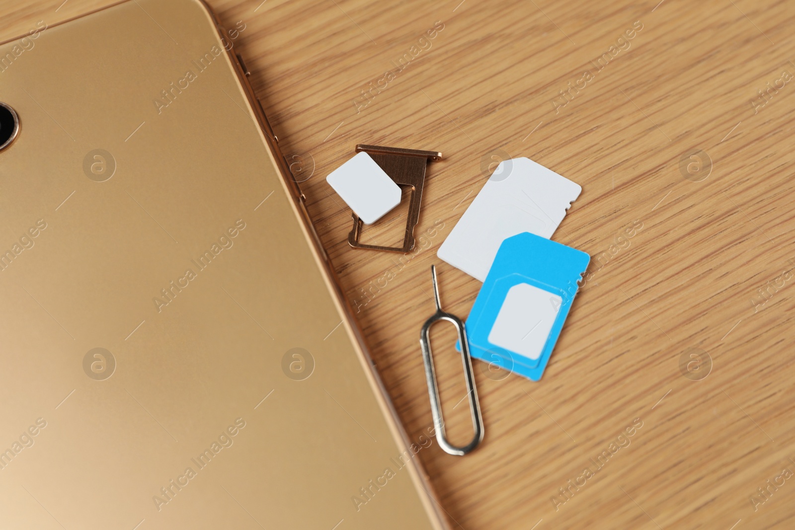 Photo of SIM cards, mobile phone and ejector tool on wooden table, flat lay