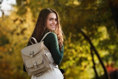 Young woman with stylish beige backpack in park, space for text