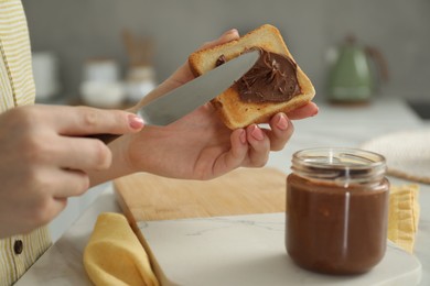 Photo of Woman spreading tasty nut butter onto toast at table, closeup