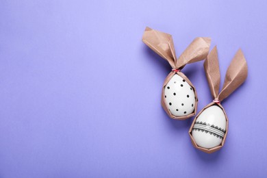 Easter bunnies made of craft paper and eggs on purple background, flat lay. Space for text