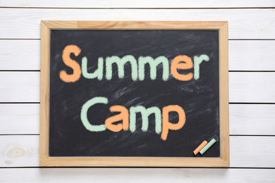 Blackboard with text SUMMER CAMP on white wooden background, top view