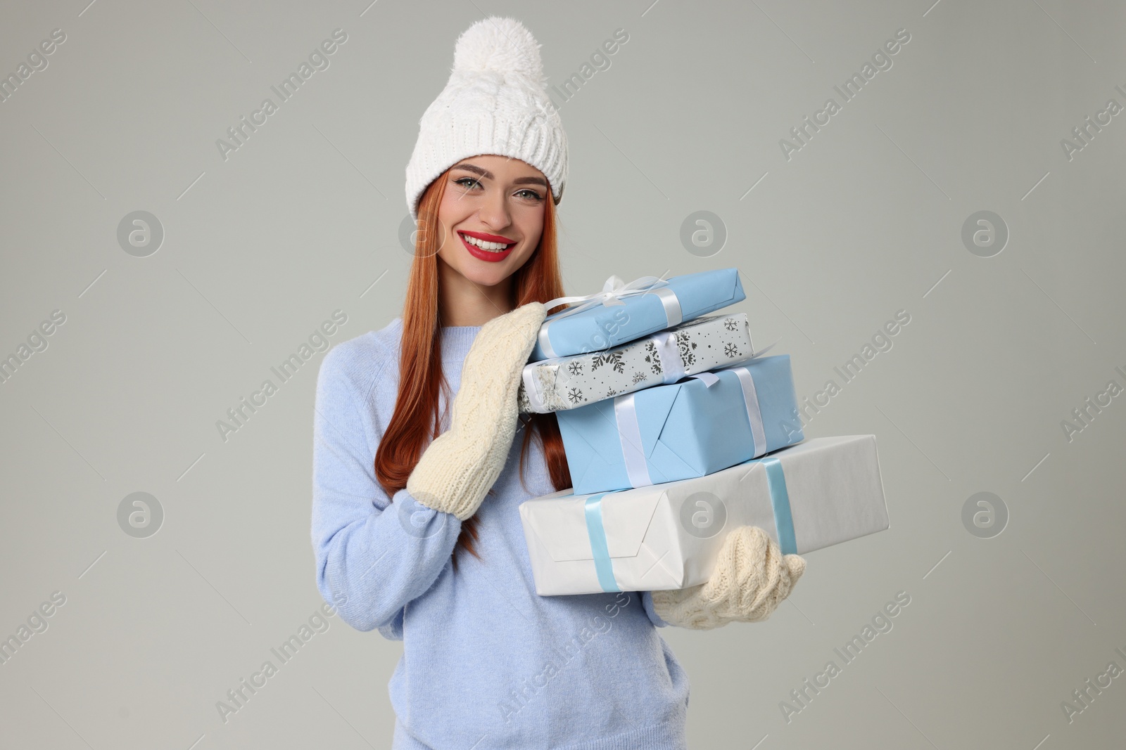 Photo of Young woman in hat and sweater with Christmas gifts on light grey background