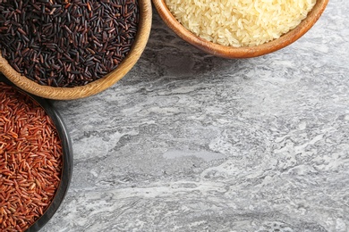 Flat lay composition with brown and other types of rice in bowls on grunge background. Space for text