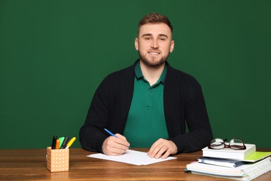 Portrait of young teacher at table against green background