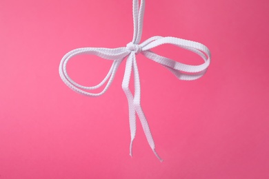 Photo of White shoe laces tied in bow on pink background