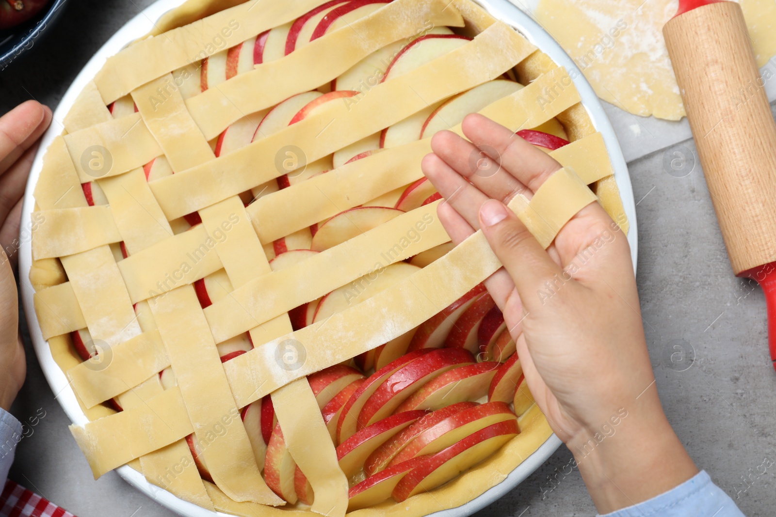 Photo of Woman decorating raw apple pie at grey table, top view