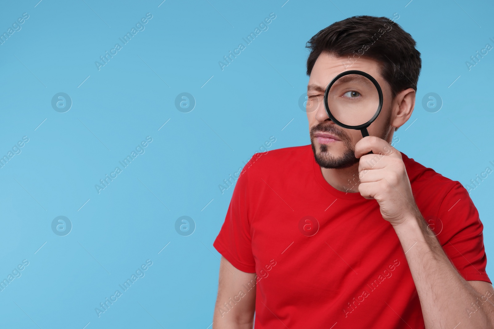 Photo of Handsome man looking through magnifier glass on light blue background. Space for text