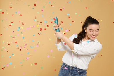 Photo of Young woman blowing up party popper on light brown background