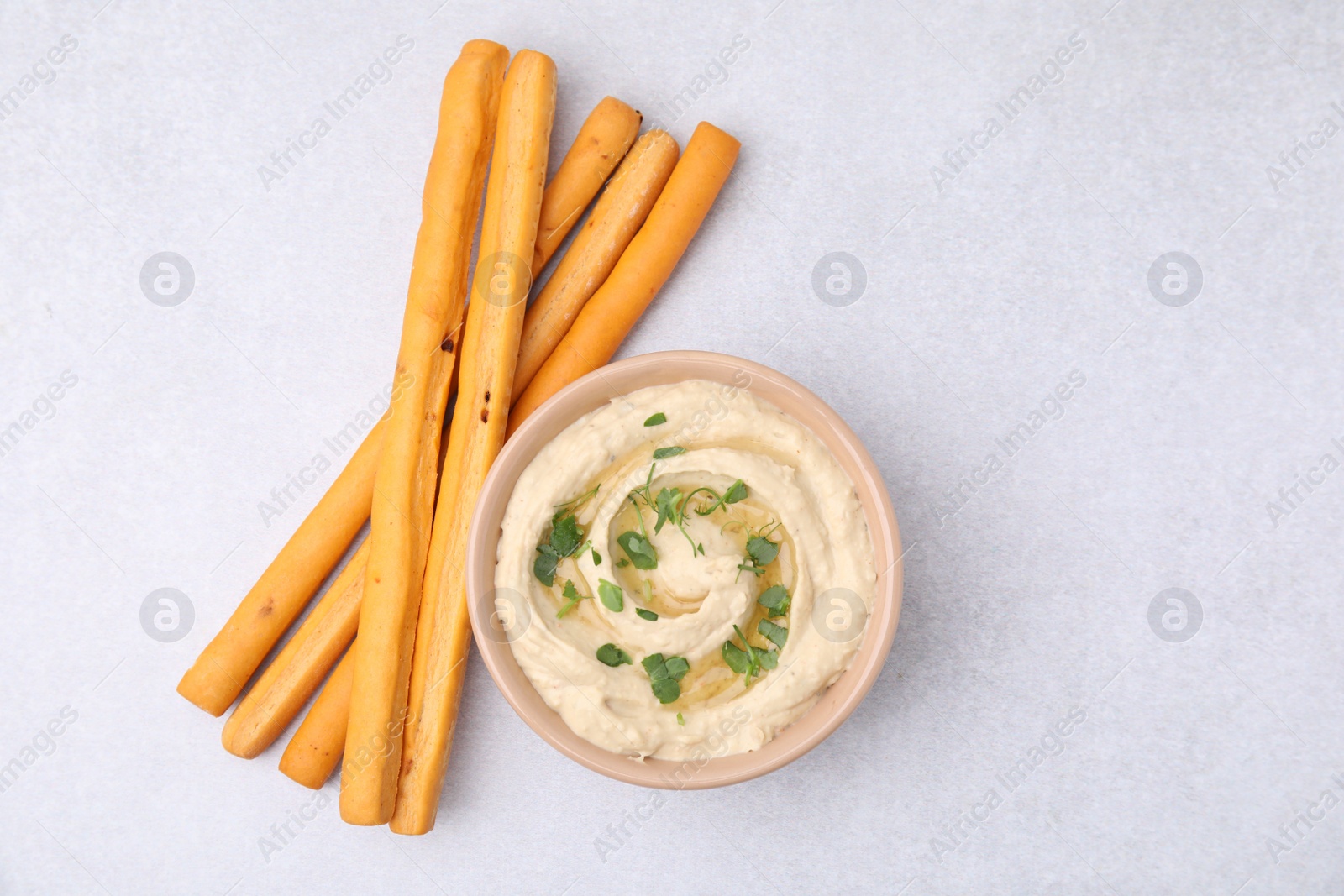 Photo of Delicious hummus with grissini sticks on light grey table, flat lay