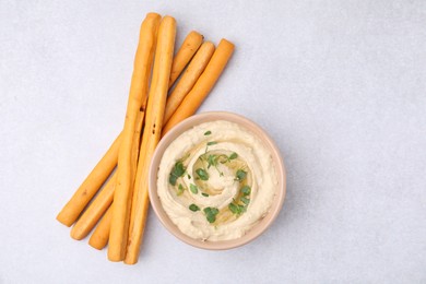 Delicious hummus with grissini sticks on light grey table, flat lay