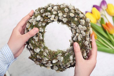 Woman holding wreath made of beautiful willow branches on blurred background, closeup