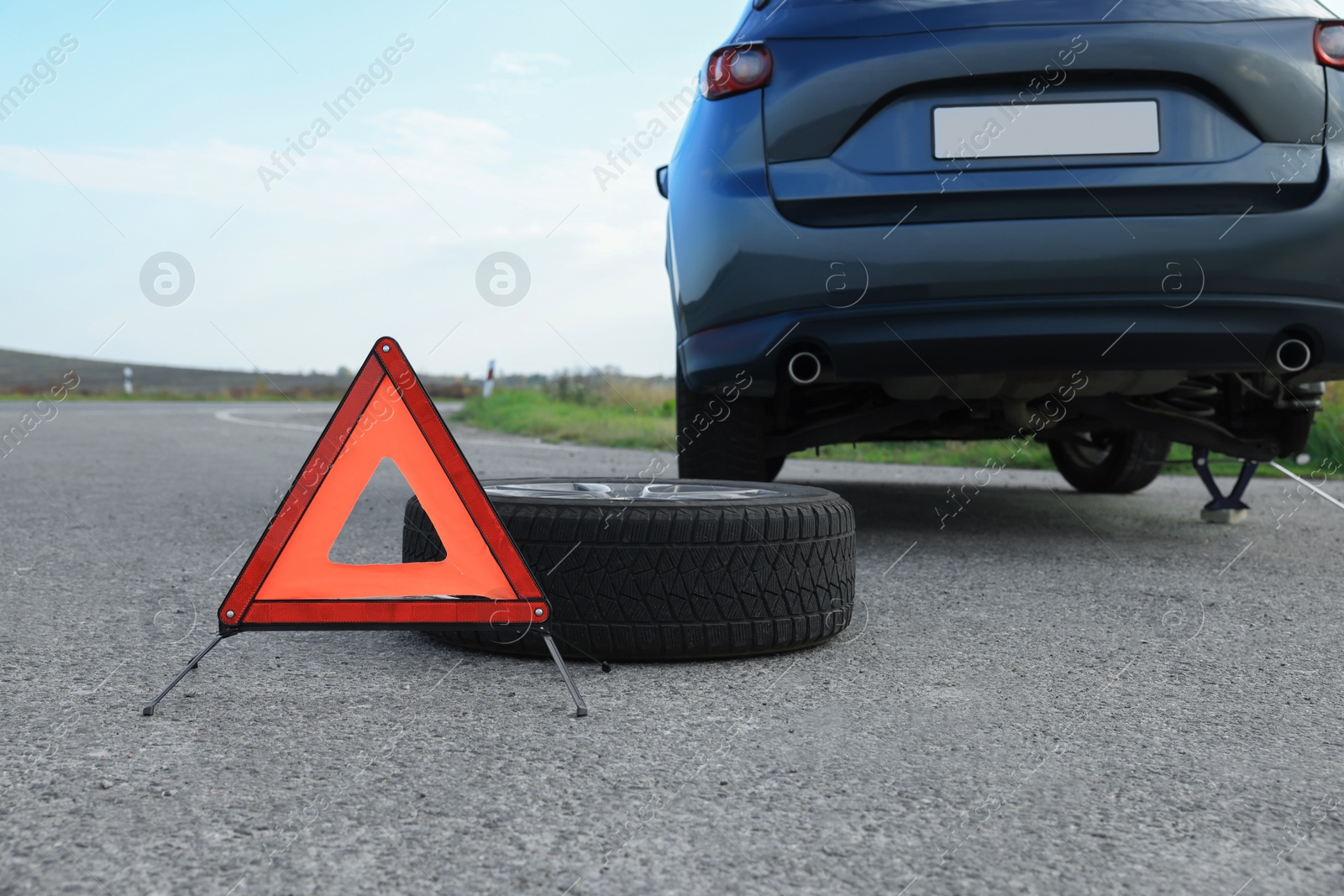 Photo of Emergency warning triangle and tire near car on roadside