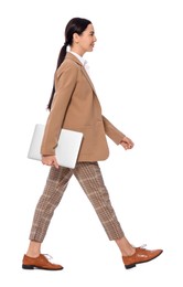 Young businesswoman with laptop walking on white background