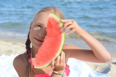 Cute little girl holding slice of juicy watermelon on beach