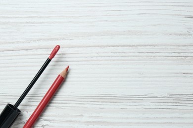 Lip pencil and brush of liquid lipstick on white wooden table, flat lay. Space for text