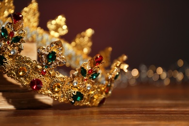 Photo of Beautiful golden crown and fairy lights on wooden table, closeup. Fantasy item