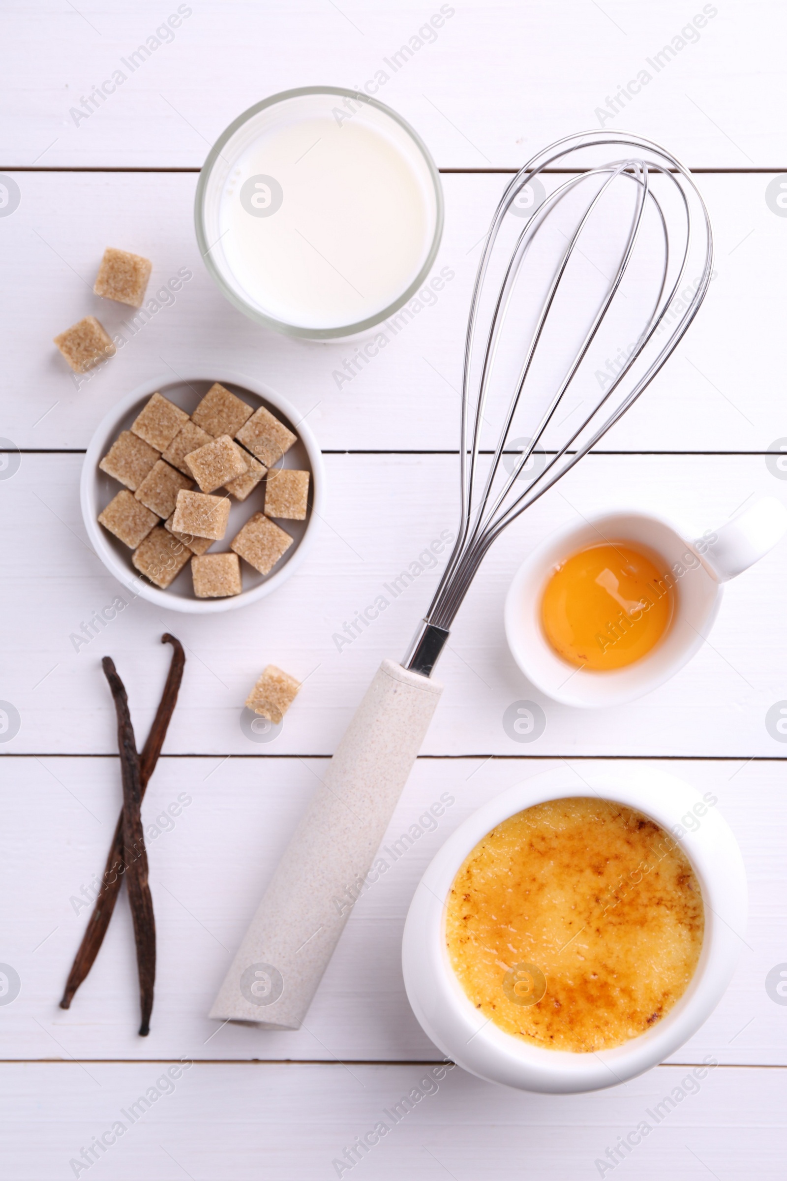 Photo of Delicious creme brulee in bowl and ingredients on white wooden table, flat lay
