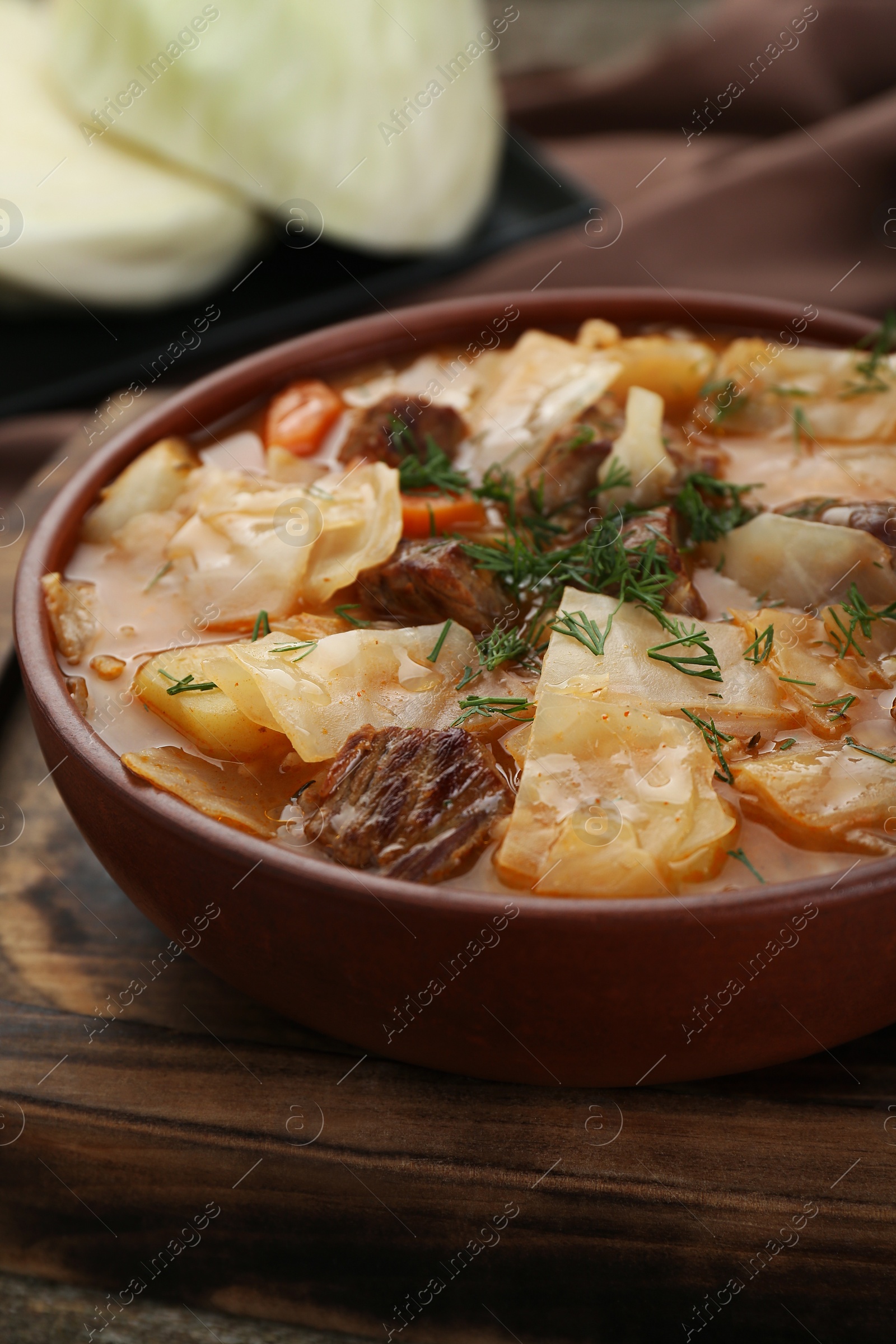 Photo of Tasty cabbage soup with meat, carrot and dill on wooden table, closeup