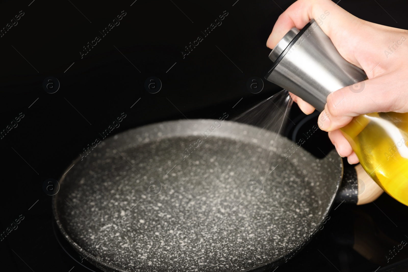 Photo of Woman spraying cooking oil onto frying pan on stove, closeup