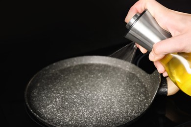 Woman spraying cooking oil onto frying pan on stove, closeup