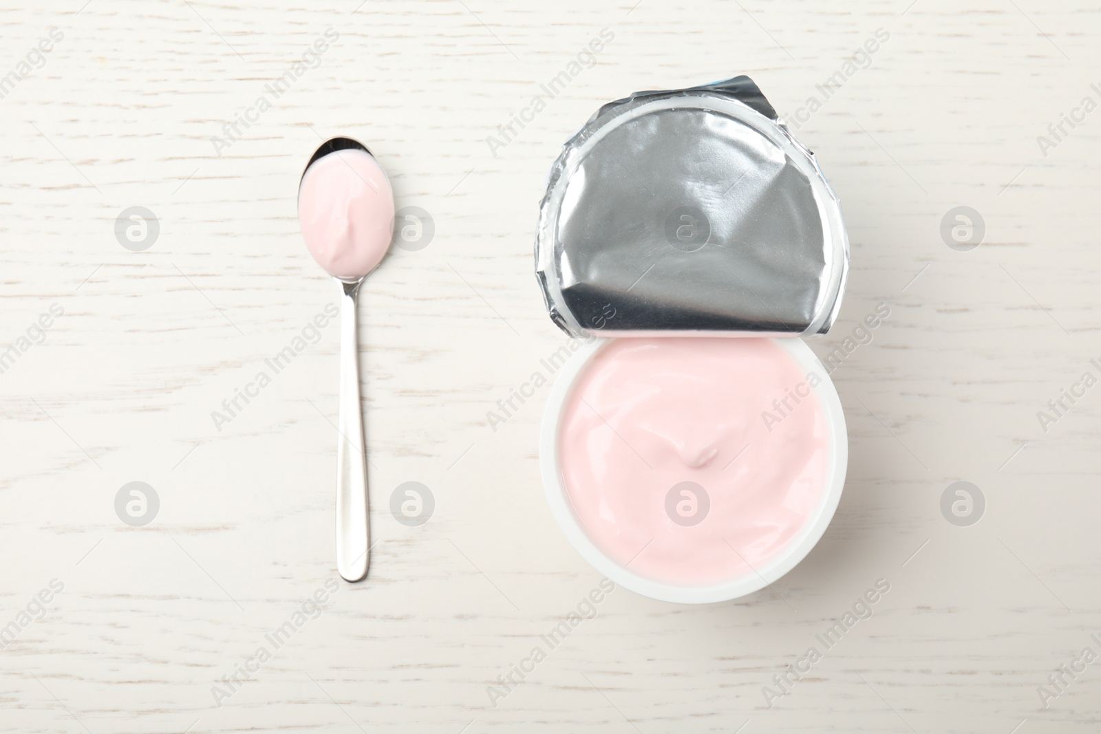 Photo of Package of fresh yogurt and spoon on white wooden background