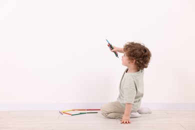 Photo of Little boy with colorful pencils near white wall indoors. Space for text