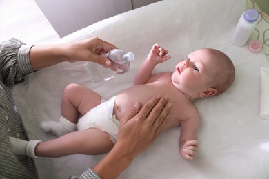 Photo of Mother massaging her baby with oil on changing table indoors, above view