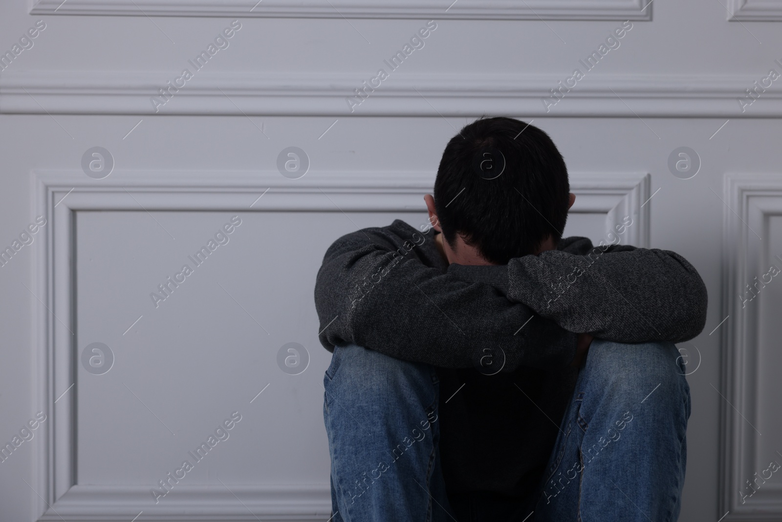 Photo of Sad man sitting near white wall indoors, space for text