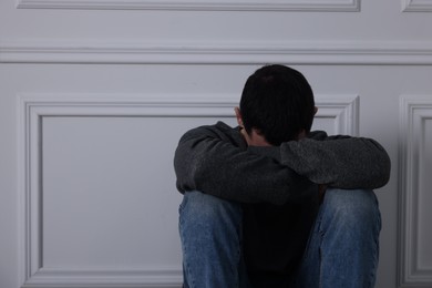 Photo of Sad man sitting near white wall indoors, space for text