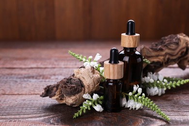Photo of Essential oils, flowers and tree branch on wooden table, closeup. Space for text