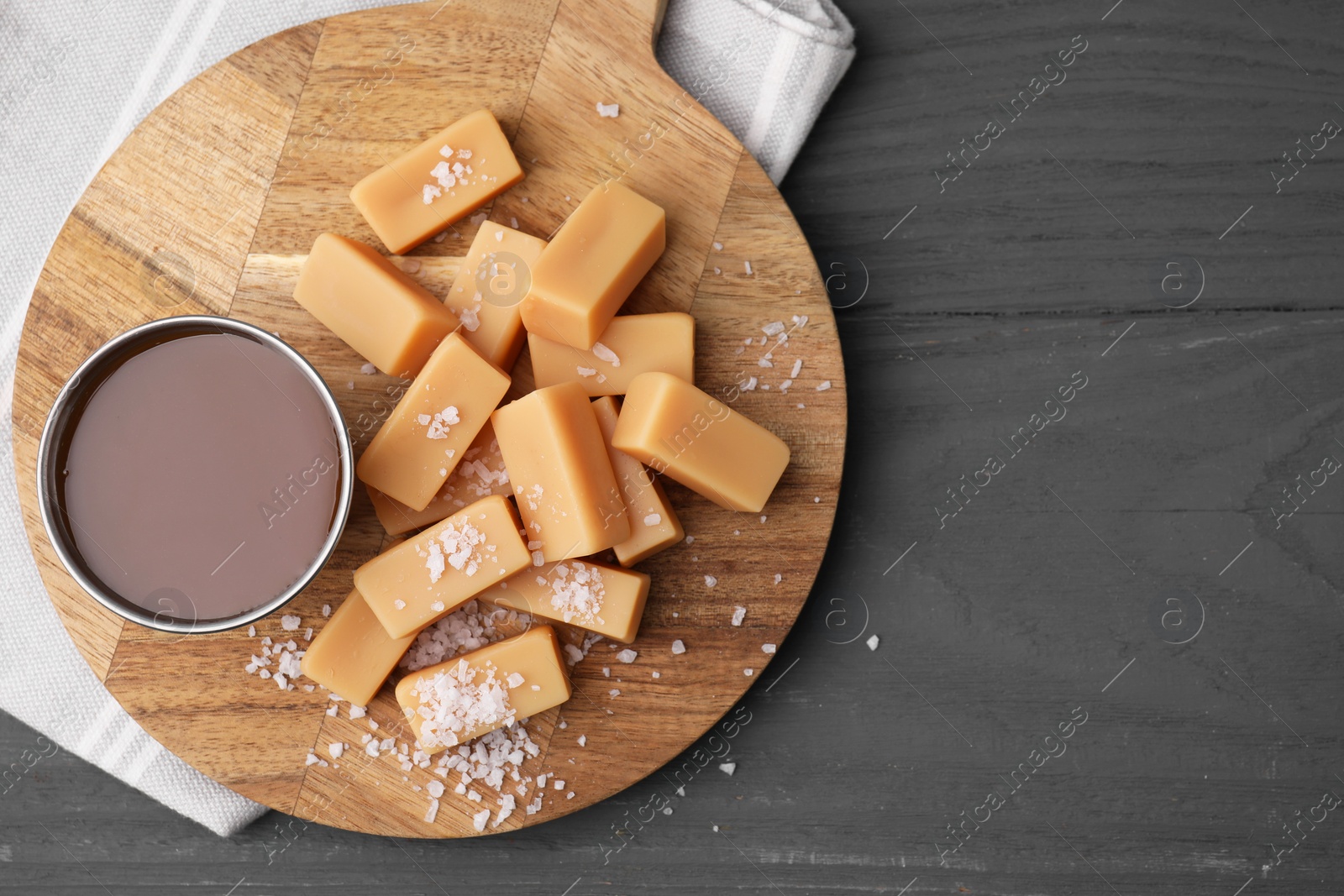 Photo of Yummy caramel candies and sea salt on wooden table, top view. Space for text