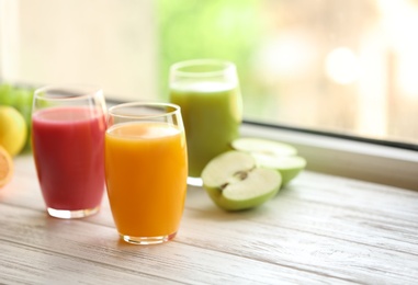 Glasses with different juices and fresh fruits on wooden window sill. Space for text