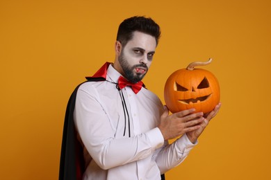 Photo of Man in scary vampire costume with fangs and carved pumpkin on orange background. Halloween celebration